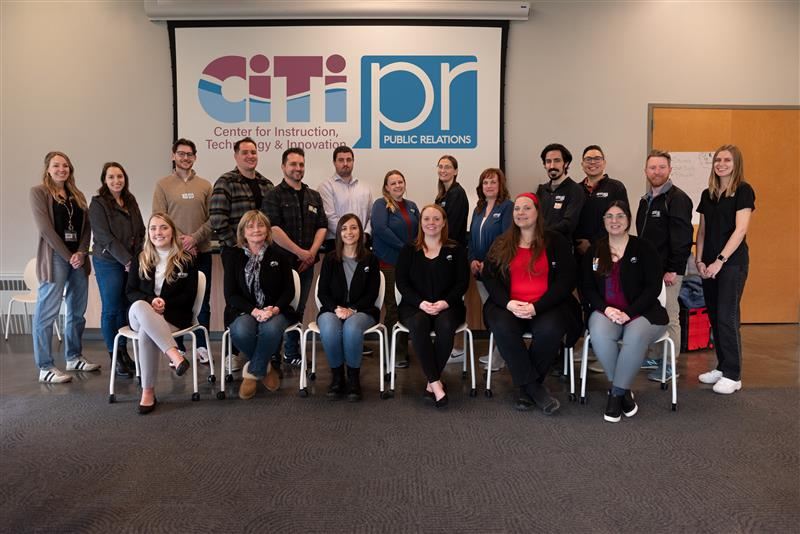 A group of 20 professionals poses in front of a "CiTi PR" sign, dressed in business casual attire.